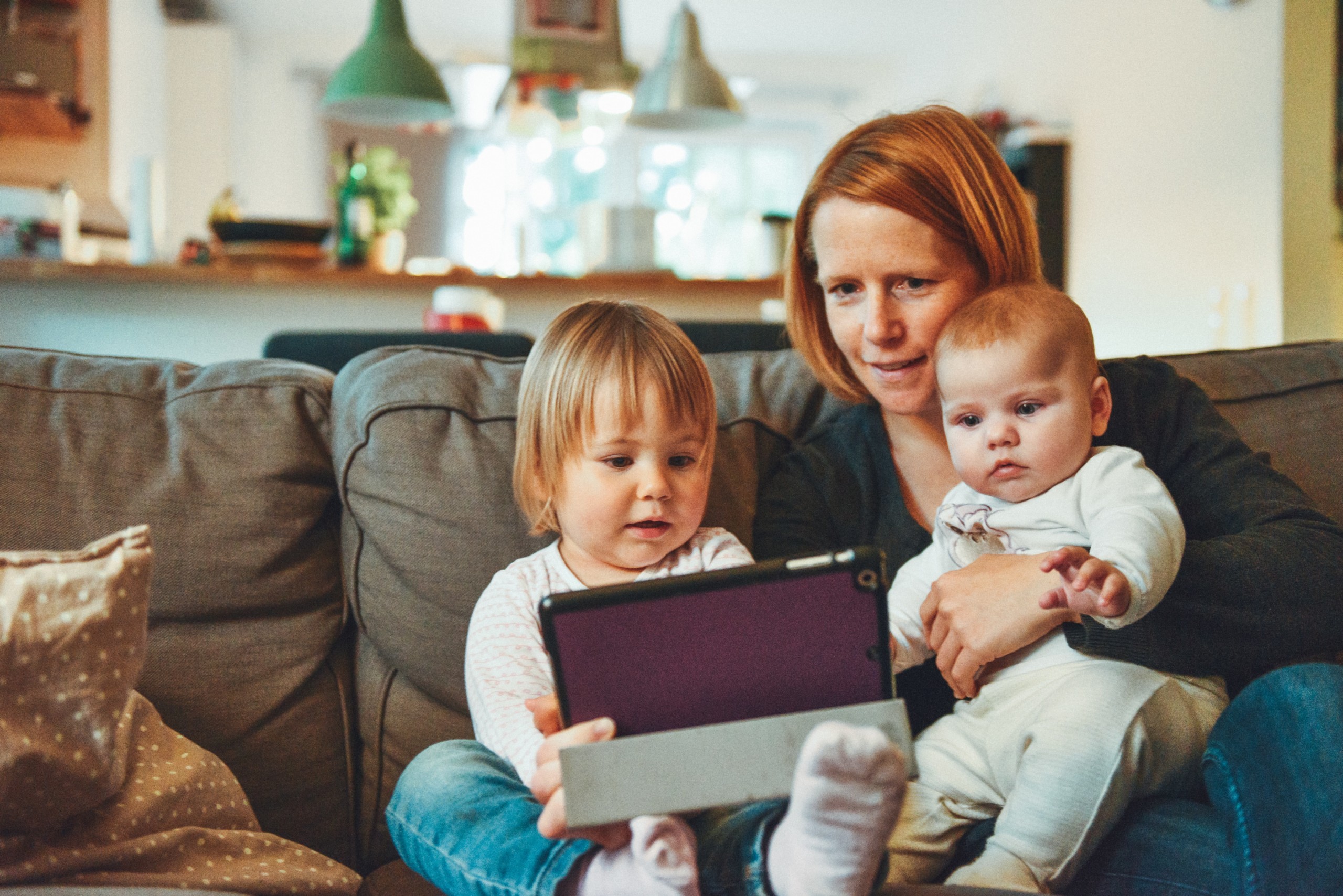 Mutter mit zwei Kleinkindern auf dem Schoß und einem Tabletgerät