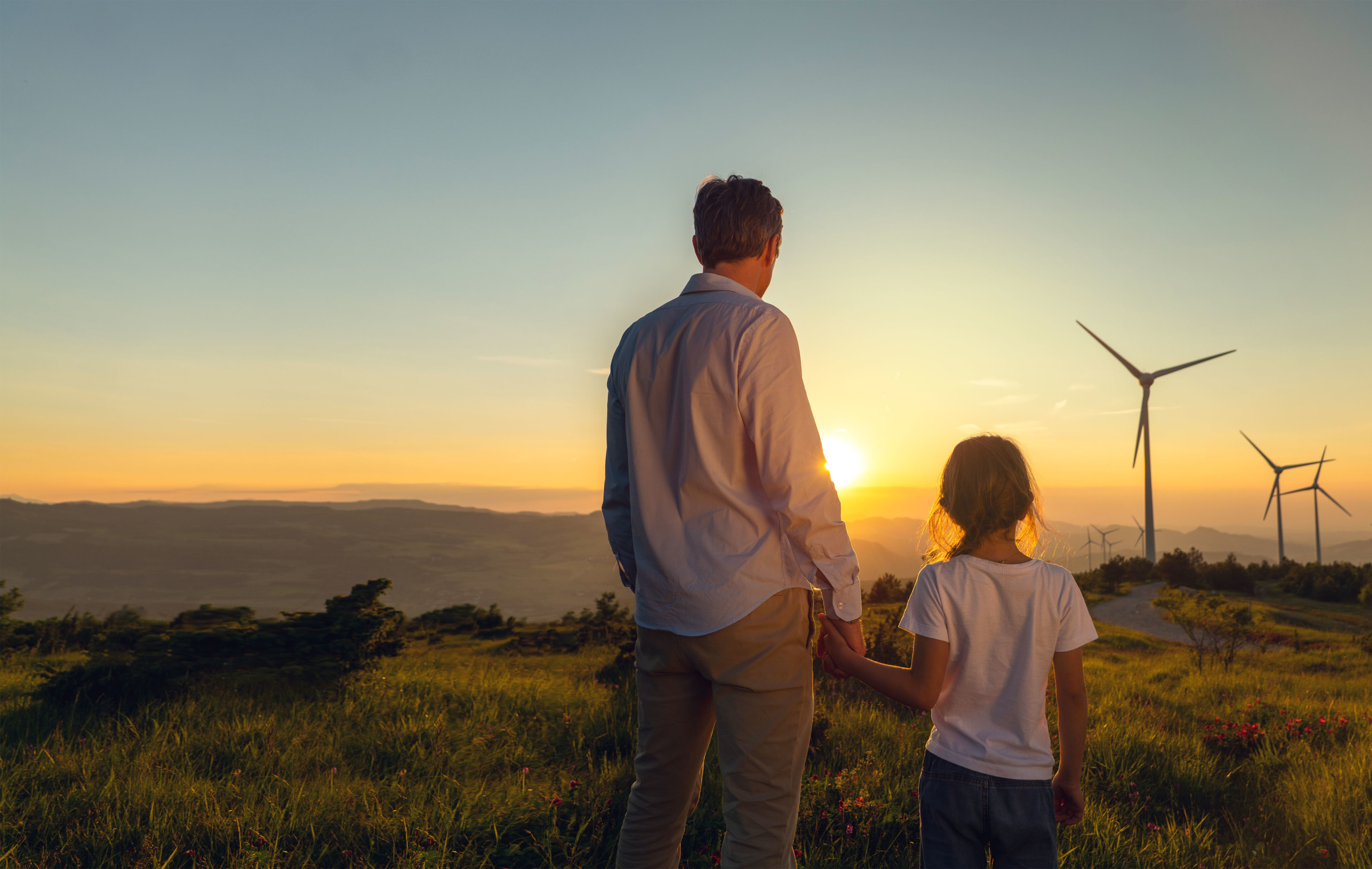 Father and daughter looking into the sun standing on a mountain