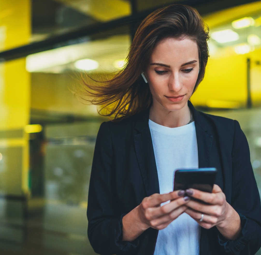 A brunette woman wearing business casual looks at her smart phone
