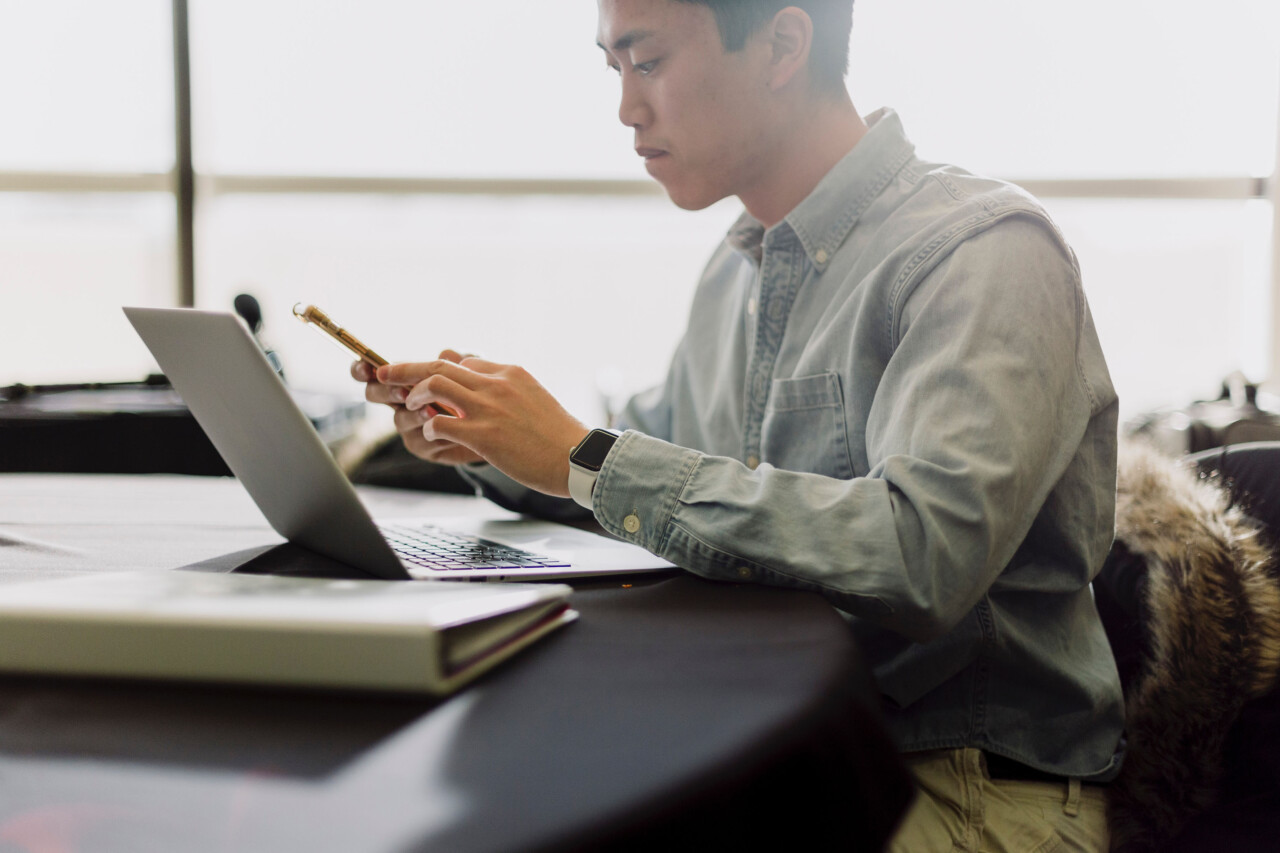Asian man with laptop looking at phone