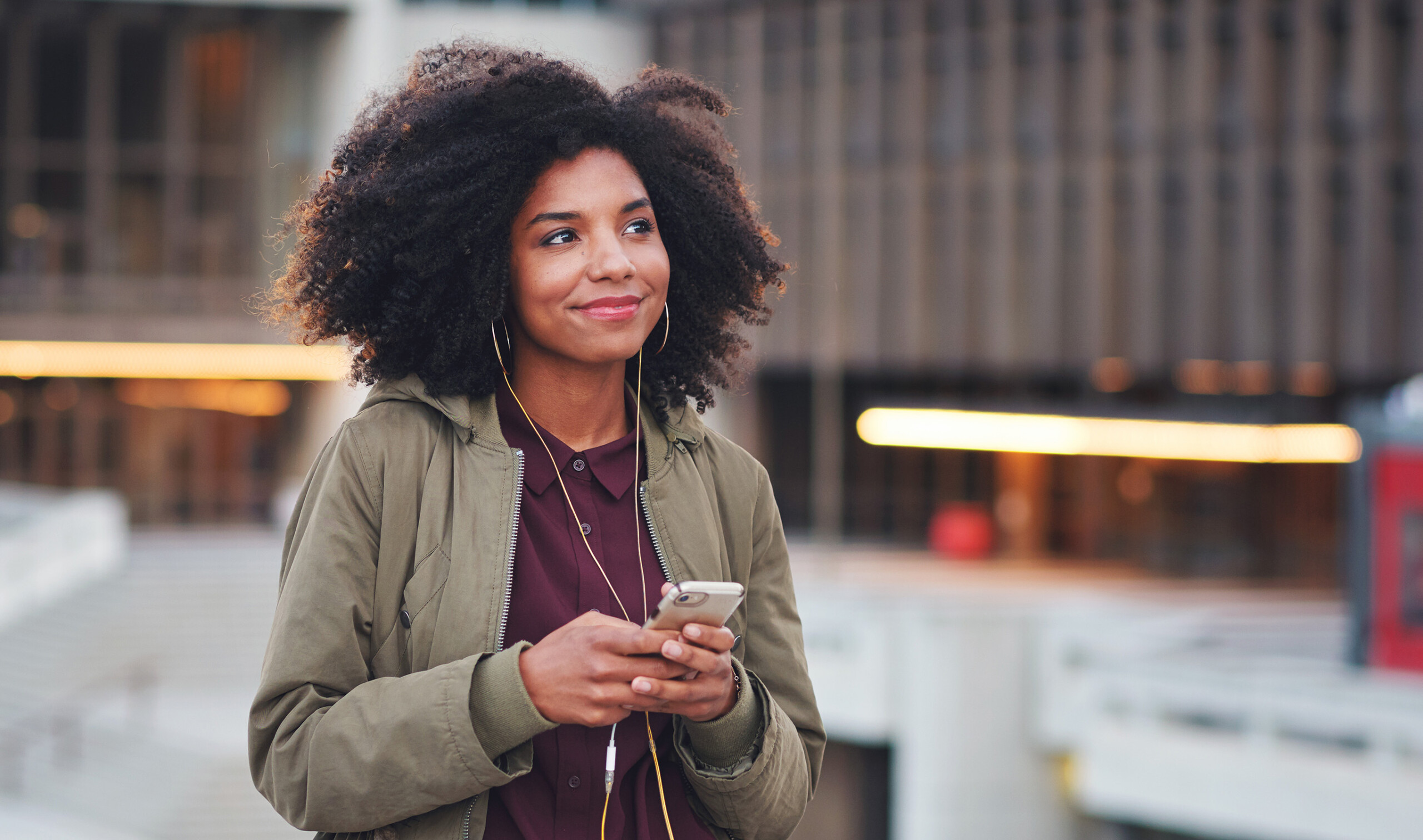 black woman in city with a mobile, listening music.